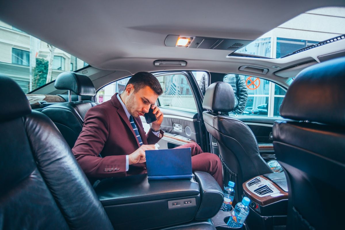 Businessman sitting in a limo while talking on his phone reading his notes and planning his day.